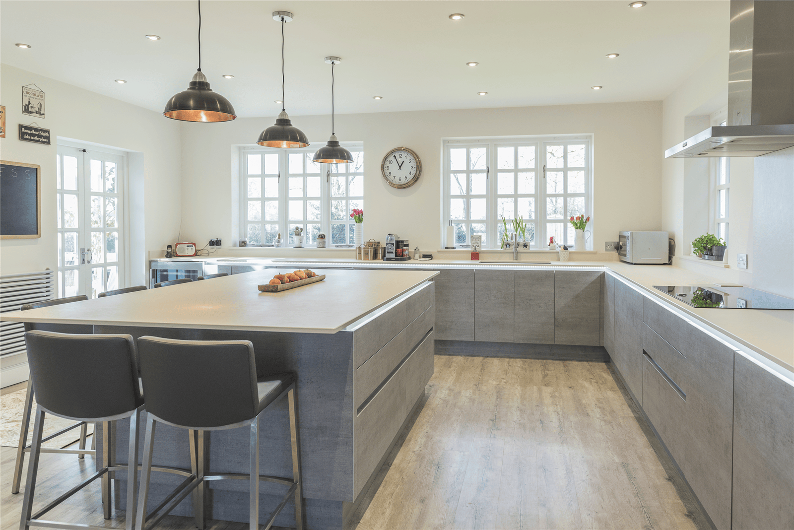 Mastercraft-bespoke-kitchens-installation-Liverpool Bespoke fitted kitchen in Liverpool featuring a large central island with breakfast bar seating, painted handleless cabinets, pendant lighting, and oak-effect flooring.